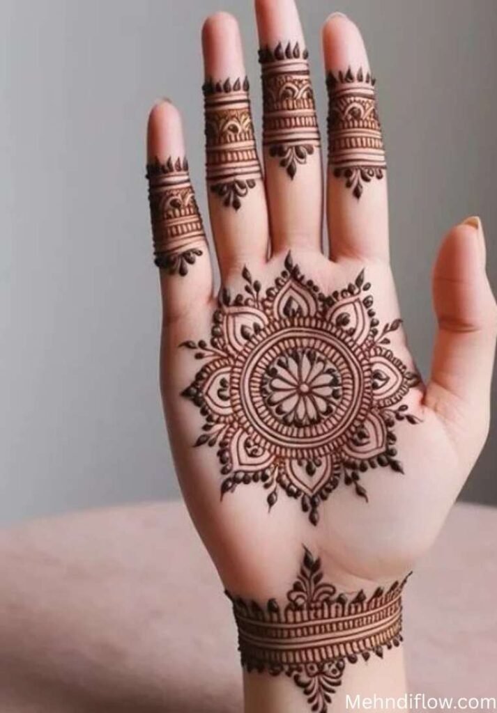 A palm-up hand showcasing a perfectly symmetrical, circular mandala mehndi design centered on the palm, paired with matching finger cuffs and a decorative wrist band.
