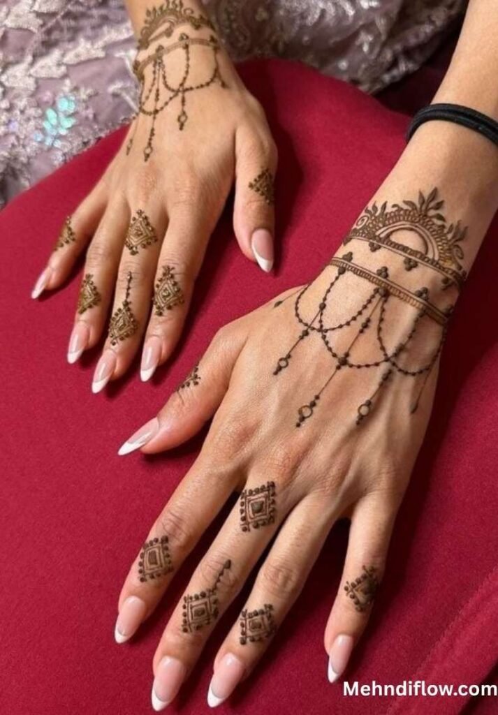 Hands on a red cushion with bracelet-style wrist mehndi and small geometric finger patterns.