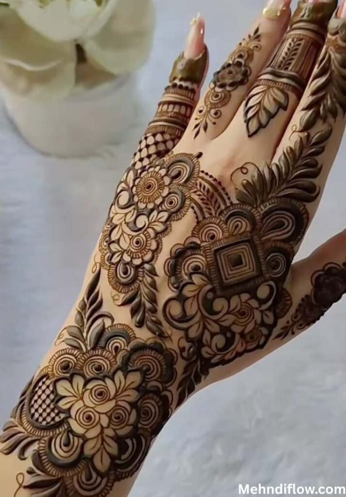 Intricate Arabic henna design on the back of a hand, showcasing a blend of central geometric shapes, dense floral shading, swirling vines, and detailed netting patterns on the fingers.