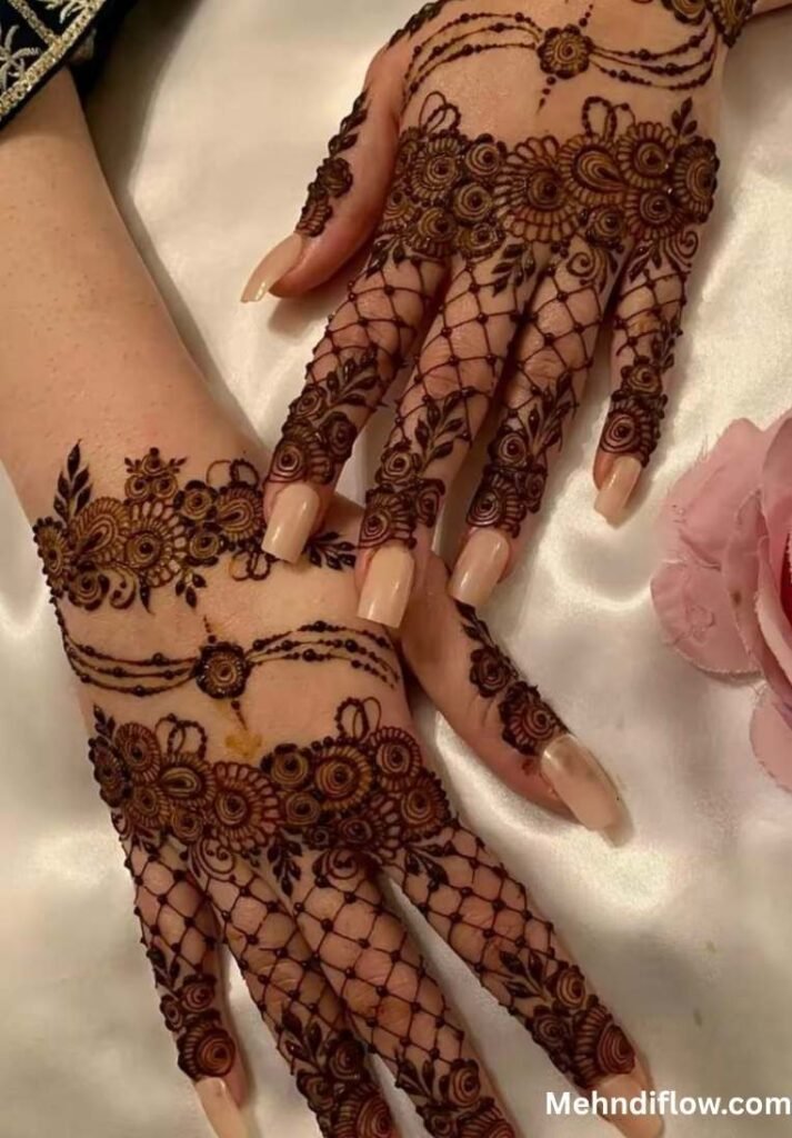 A close-up of hands displaying a fusion mehndi style, combining intricate net (lattice) patterns on the fingers and base of the hand with elaborate floral bands across the mid-hand and wrist.