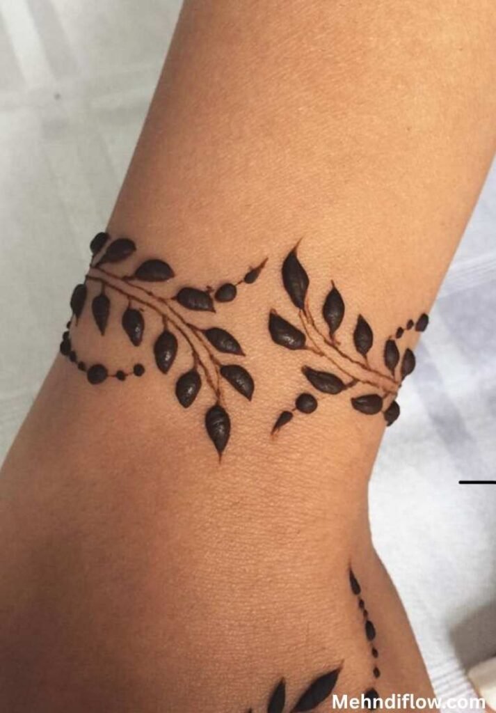 A wrist adorned with a bracelet-style mehndi design featuring delicate, interconnected leaf patterns.