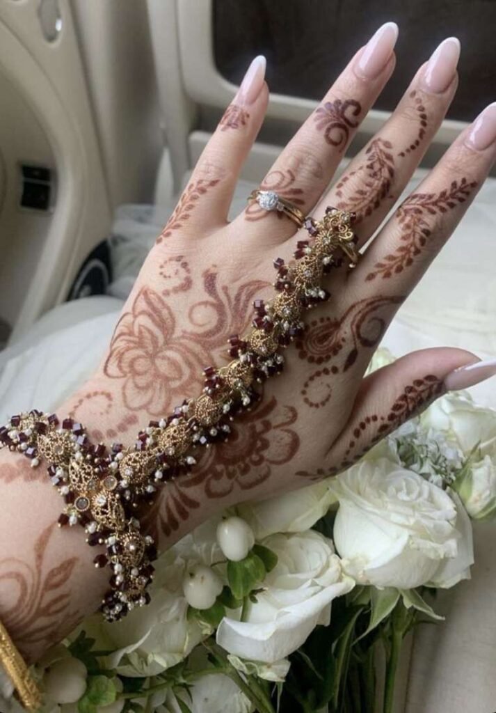 Light floral back hand mehndi styled with an ornate gold and beaded hand harness.