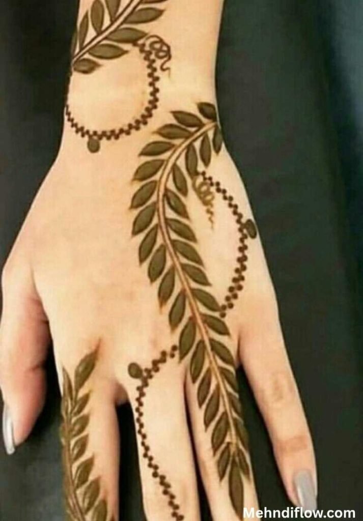 A hand showcasing a bridal leaf fusion mehndi design with prominent leaf vines and circular chain accents.