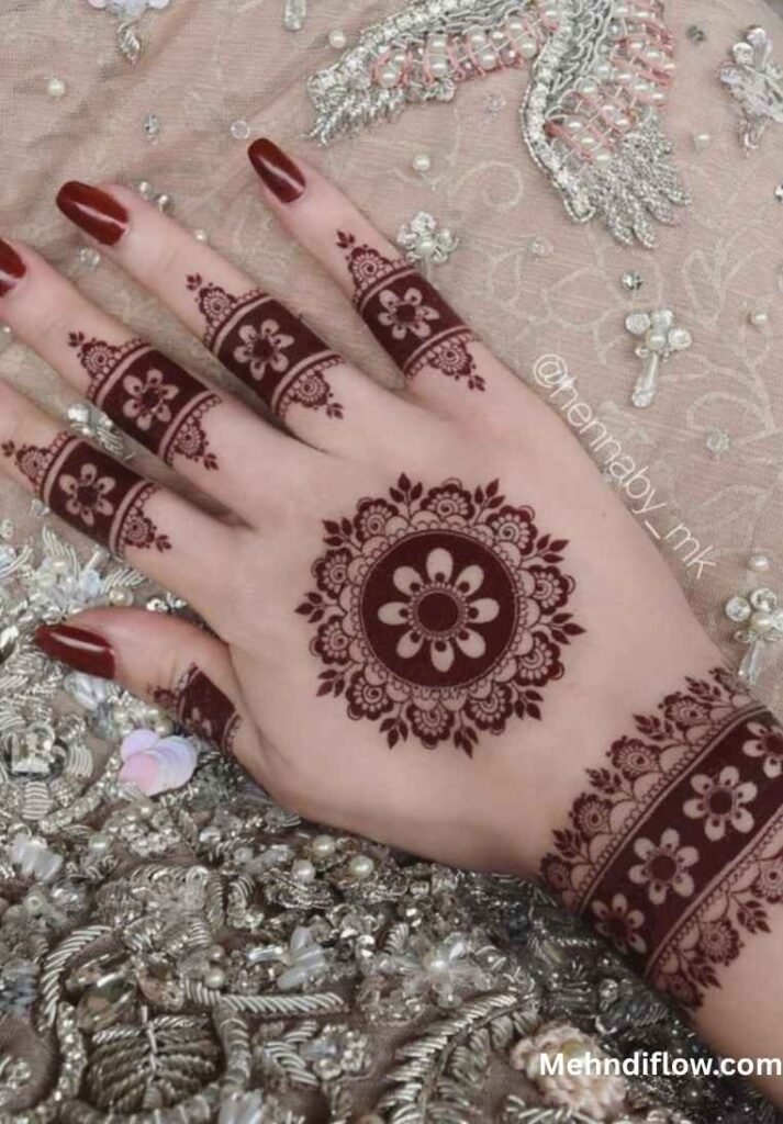 A close-up of a hand displaying a traditional round tikki mehndi style, showcasing a bold, central circular mandala design paired with an intricate, ornate band around the wrist and matching finger detailing.