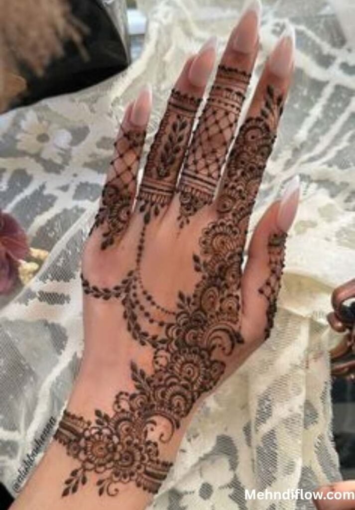 A close-up view of two hands displaying a dense and intricate bridal mehndi design, characterized by elaborate scalloped borders, traditional mandalas, and finely detailed net work across the hands and wrists.