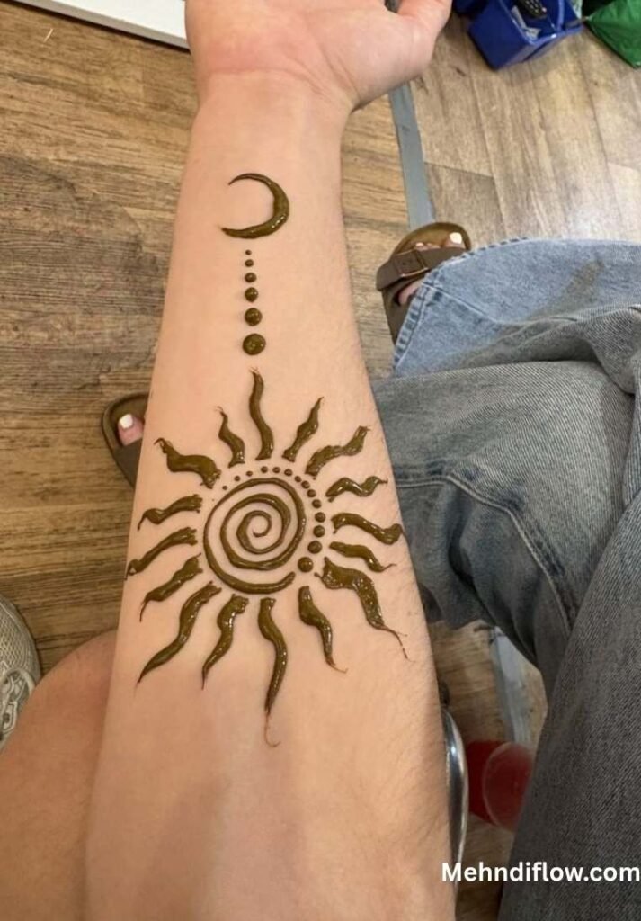 A forearm displaying a minimalist, spiritual-themed mehndi design consisting of a central spiral sun motif connected to a small crescent moon symbol by a string of dots.
