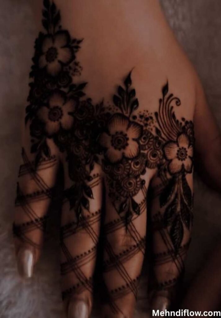 A close-up of a hand showcasing a bold, finger-focused mehndi design characterized by large floral elements at the base of the fingers and fine, cross-hatched grid lines extending down to the fingertips.