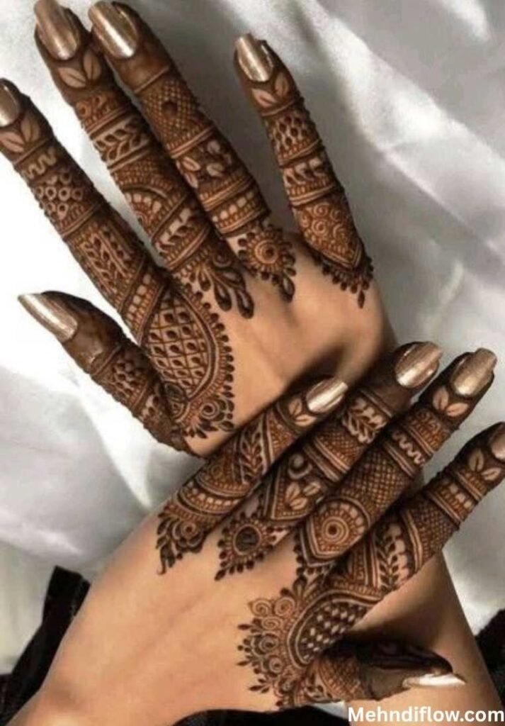 A close-up of a hand displaying intricate, finger-focused mehndi patterns featuring detailed geometric and floral motifs that cover the entire length of the fingers.