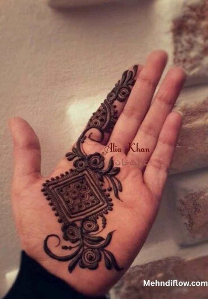 A palm displaying an intricate, ornamental henna design with a central square mandala, accented by flowing floral vines and elegant scrollwork.