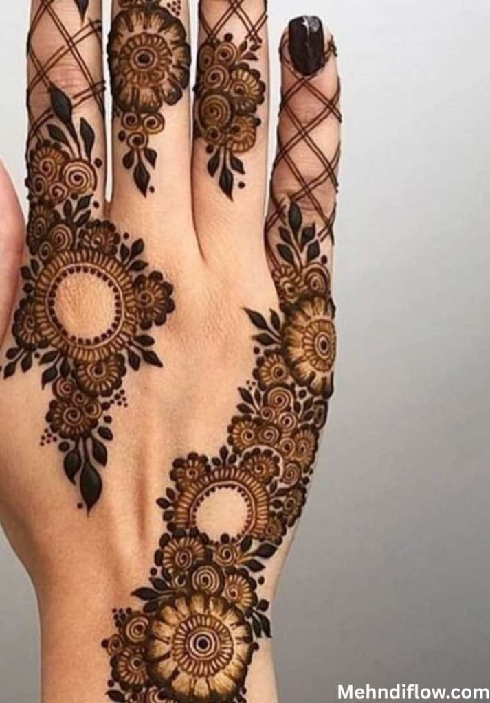 A close-up of a hand featuring a bold floral trail mehndi design composed of large, circular mandala-style flowers connected by delicate vines, with a grid pattern on the fingers.