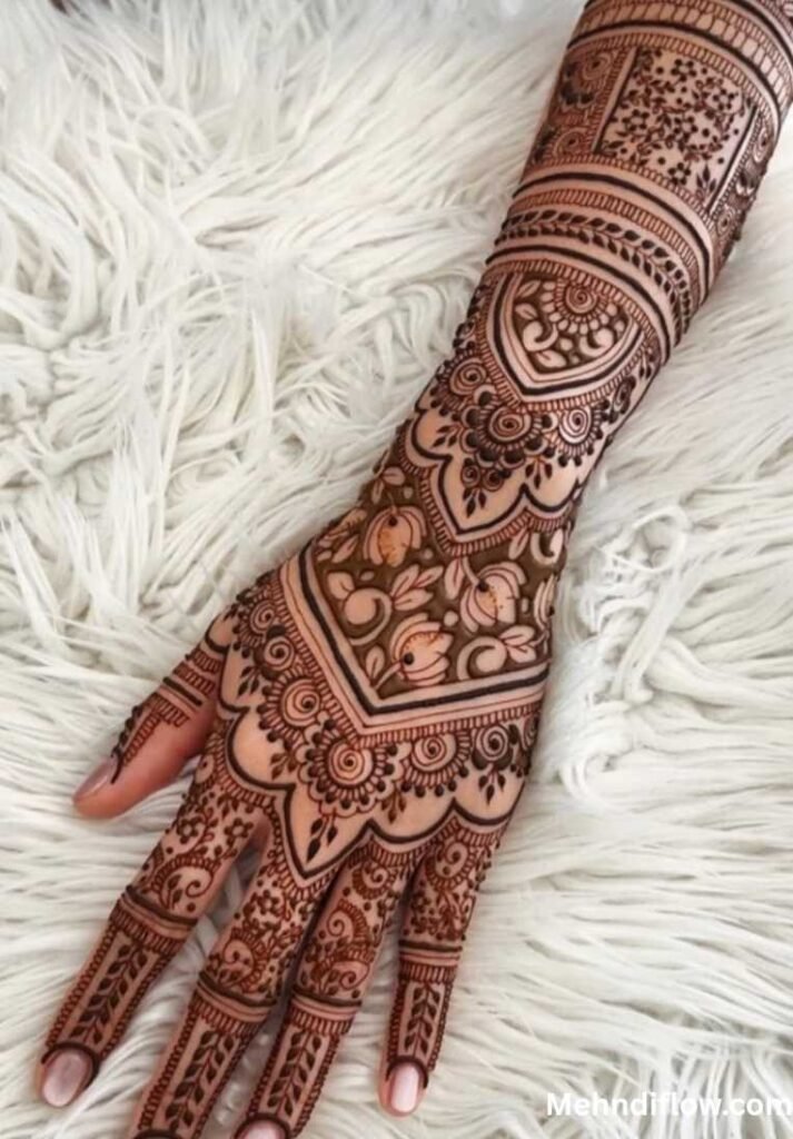 A close-up of a hand with a sophisticated bridal mehndi design, showcasing a seamless fusion of floral motifs, geometric lattice work, and detailed bands reaching up the forearm.