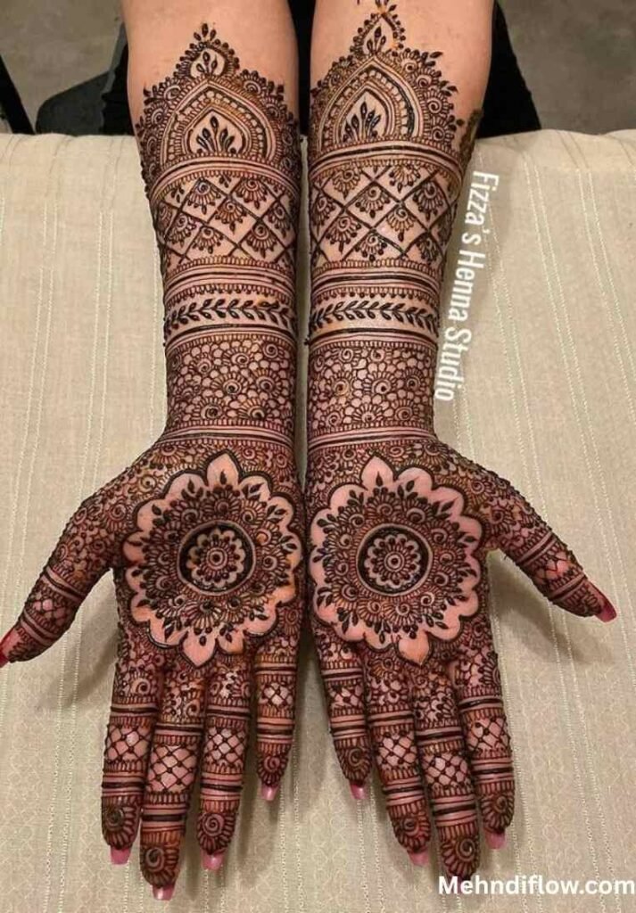 A pair of palms displaying elaborate full-hand mehndi designs, featuring large, intricate central mandalas surrounded by dense, detailed net patterns and floral borders extending down the fingers.