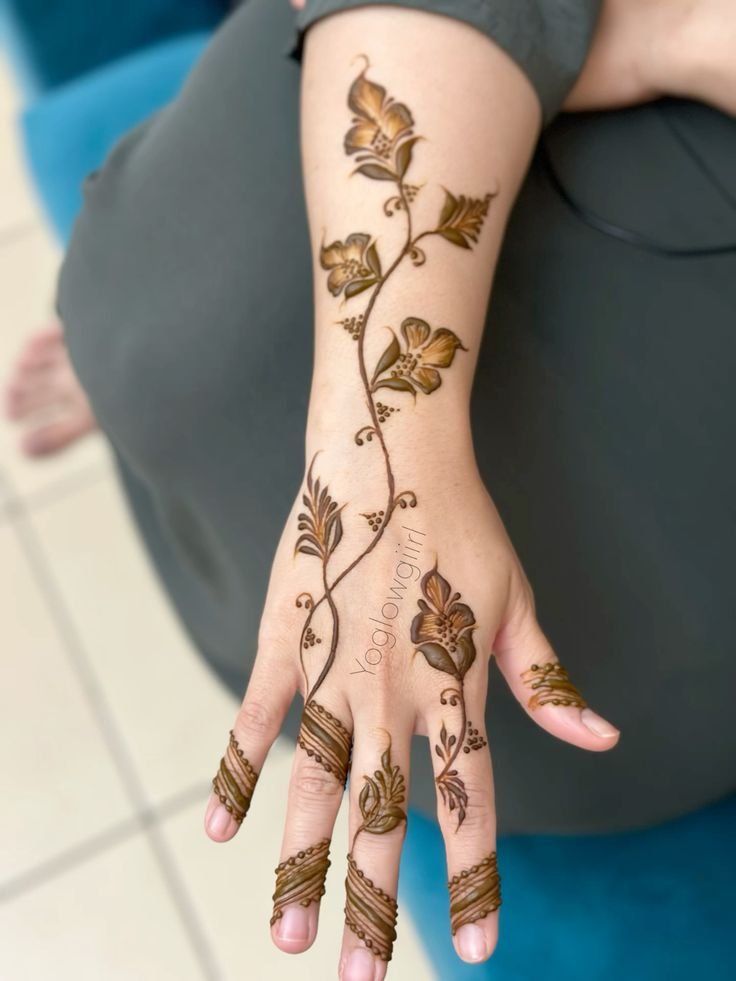 A hand showcasing a flowing floral and leaf mehndi vine design extending from the wrist to the fingers.