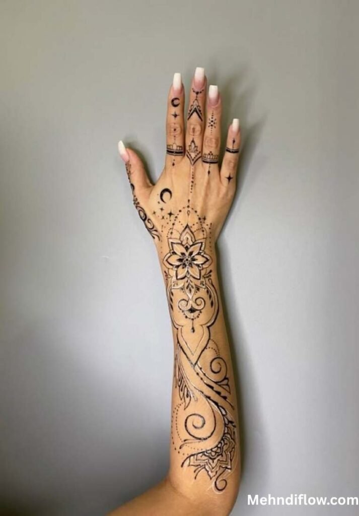 Elegant celestial and geometric half arm mehndi design featuring a central mandala flower on the wrist, delicate finger accents with crescent moons and stars, and sweeping vine details traveling down the forearm.
