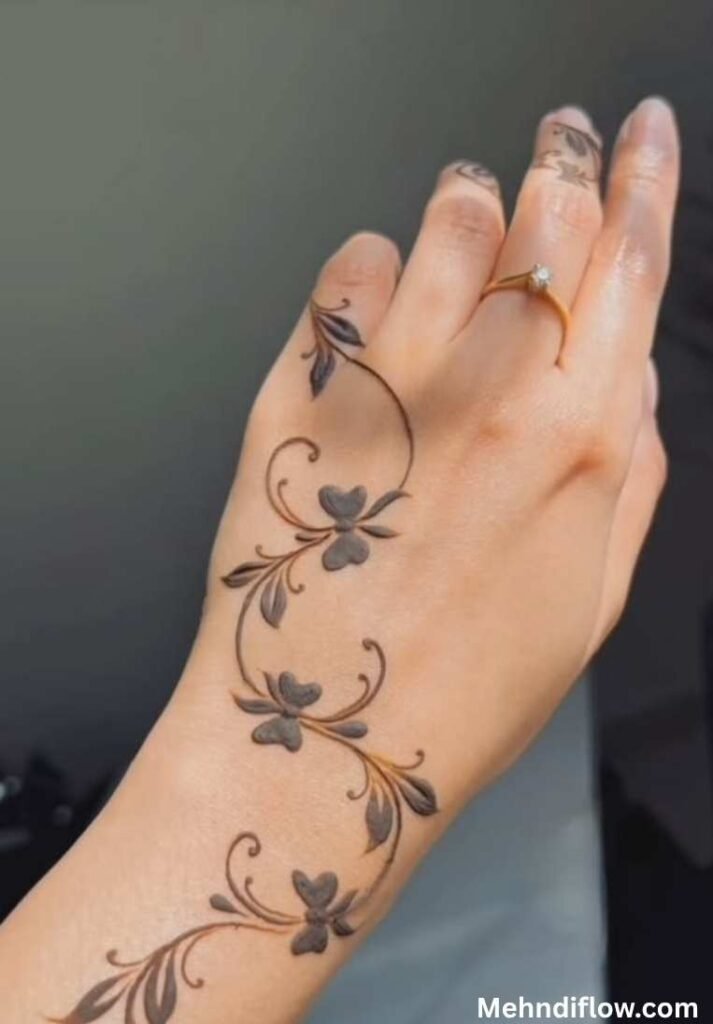 A hand featuring a bold, artistic leaf mehndi pattern spreading across the wrist and fingers.