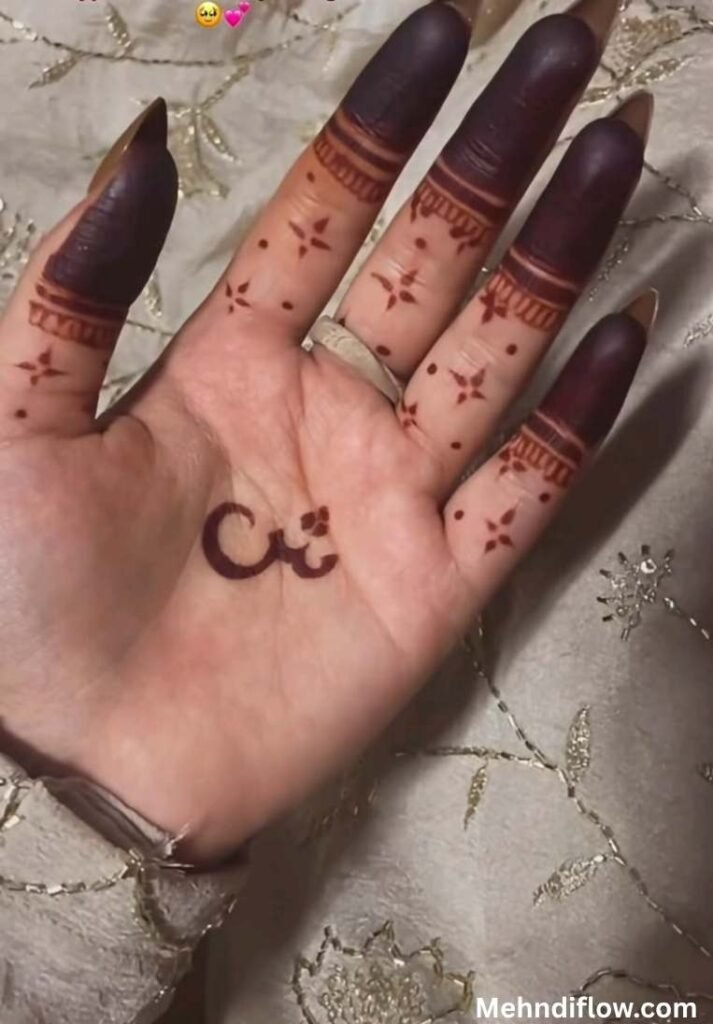 "Close up of a person's palm with a small, minimalist Arabic script mehndi design in the center, delicate star patterns dotted across the fingers, and dark-stained finger tips."
