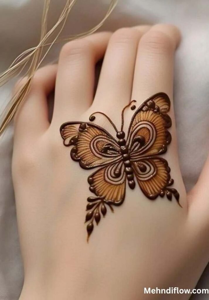 Intricate, symmetrical shaded butterfly henna design centered on the back of the hand with small leafy motifs.