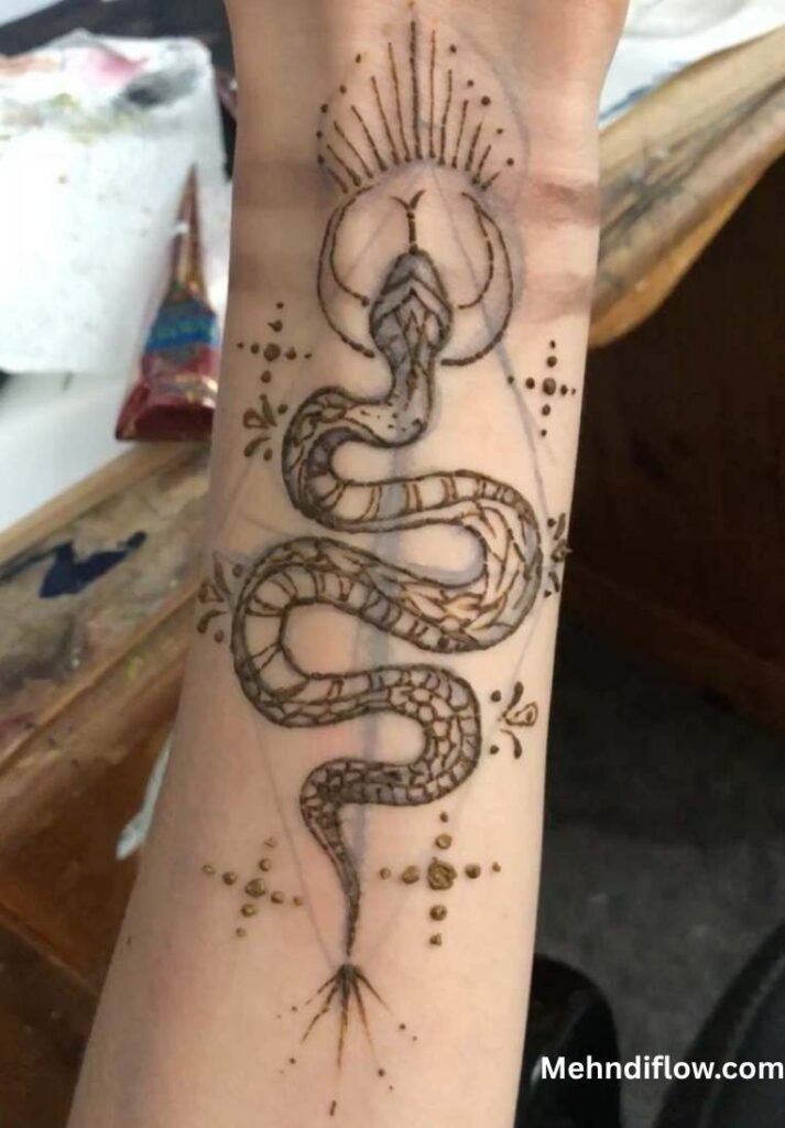 A wrist or forearm displaying a detailed tattoo-inspired mehndi design of a stylized snake surrounded by geometric lines, small dots, and a radiant sunburst element at the top.
