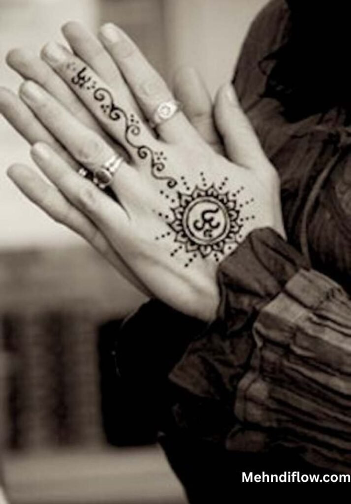 A hand joined in a prayer gesture, featuring a mehndi design on the back of the hand that incorporates a central "Om" symbol surrounded by a sunburst pattern and delicate finger ornamentation.