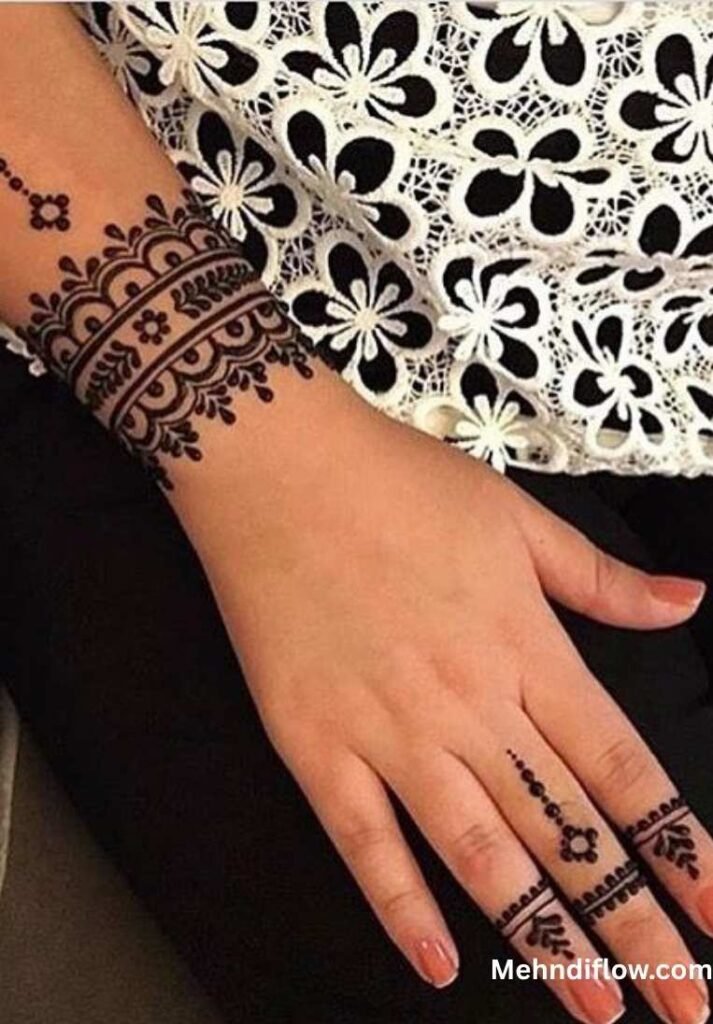 A wrist displaying a broad, ornate mehndi band with intricate decorative borders and matching geometric patterns on the fingers.