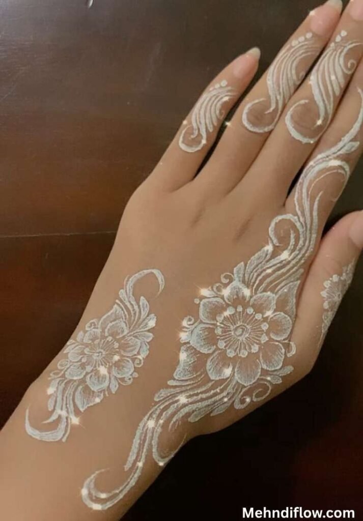 Bold Arabic-style white mehndi design featuring a prominent central flower with thick, sweeping swirls and trailing floral patterns along the back of the hand and fingers.