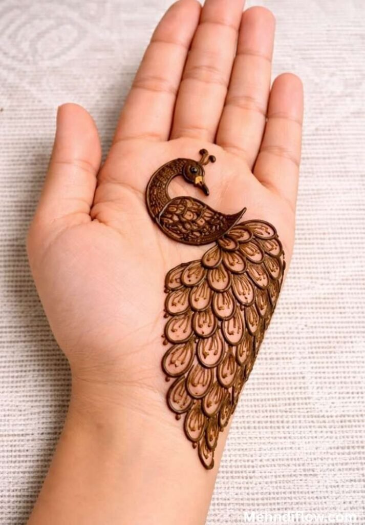 A bold, centered peacock henna design on the palm with a heavy, detailed feather tail flowing toward the wrist.