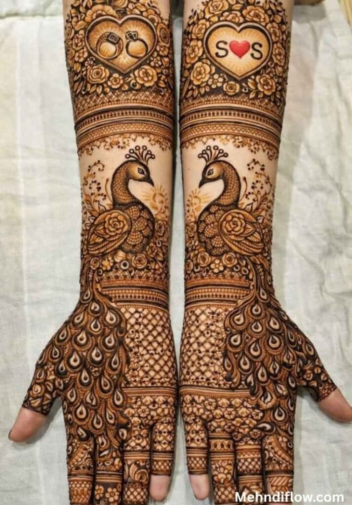 Intricate full-arm bridal henna featuring matching peacocks facing each other on the forearms, accented with initials and heart motifs.