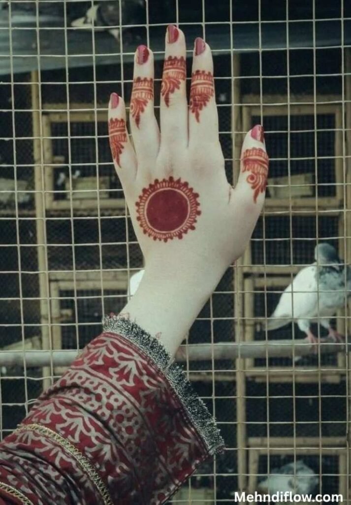 Festive Eid mandala mehndi design on the back of the hand with a deep reddish-brown central tikki circle and detailed finger patterns.