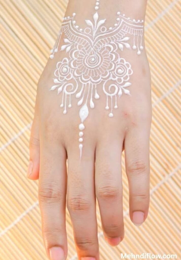 Symmetrical floral white henna design resembling a jewelry chandelier, showcasing a central mandala with elegant arches and dripping dotted details on the back of the hand.