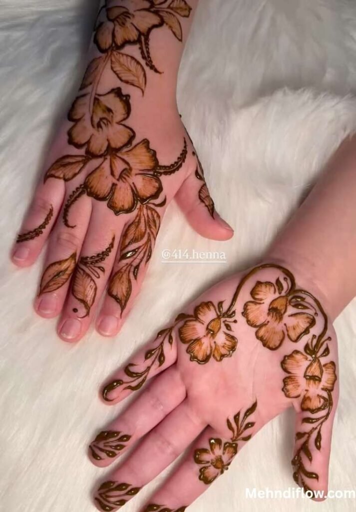 Half palm raj mehndi design featuring large shaded blossoms, sweeping leafy vines, and delicate petal details extending from the wrist across the palm and fingers.