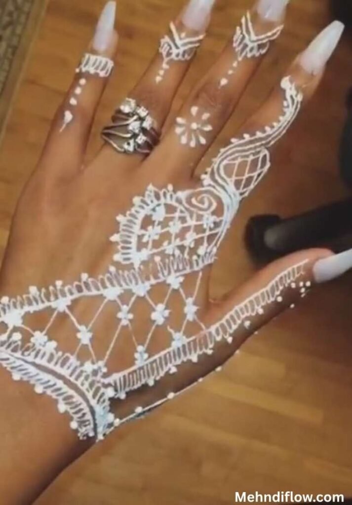 Bold jewelry-style white mehndi design featuring a criss-cross mesh hand harness with decorative floral dots, an intricate wrist cuff, and delicate finger rings.