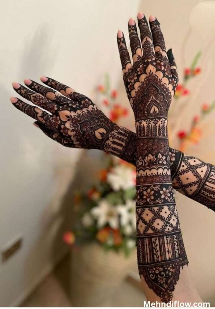Heavy, full-coverage Mughal bridal mehndi on crossed forearms and hands, showcasing intricate jaali (net) work, traditional architectural arches, and dense floral patterns.

