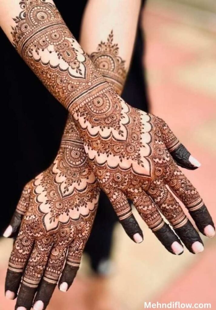 Elaborate Pakistani bridal mehndi on the back of the hands and forearms, featuring bold dome structures, scalloped lace patterns, and fully shaded fingertips.