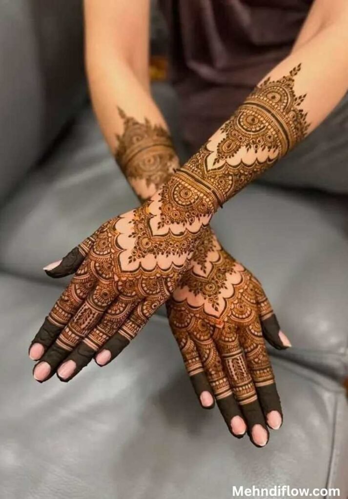 Detailed Pakistani bridal mehndi on crossed hands, highlighting a uniform geometric layout, bold central wrist cuffs, and dark, solidly filled finger tips.