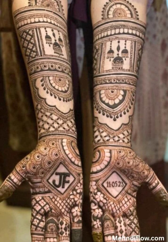 Intricate Rajasthani dulhan mehndi on open palms and forearms, featuring hanging jhumka motifs, scalloped arches, and a central diamond frame highlighting initials and a wedding date.