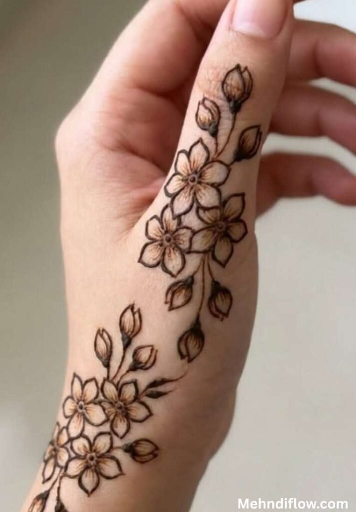 Minimalist flower trail henna art sweeping up the side of the hand and thumb with small buds.