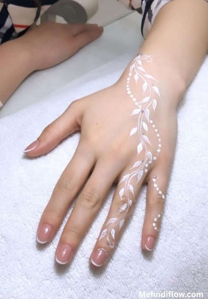 Minimalist white mehndi design featuring an elegant floral vine and delicate dotted trails cascading down the back of the hand and middle finger.