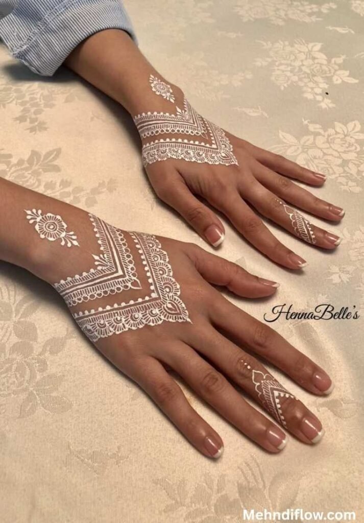 Intricate lace-style white henna design showcasing detailed geometric borders, subtle mandalas, and elegant finger patterns on the back of two hands.