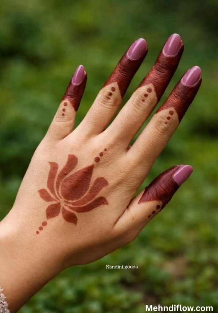 Minimalist single lotus mehndi design on the back of the hand with geometric pointed fingertip stains.