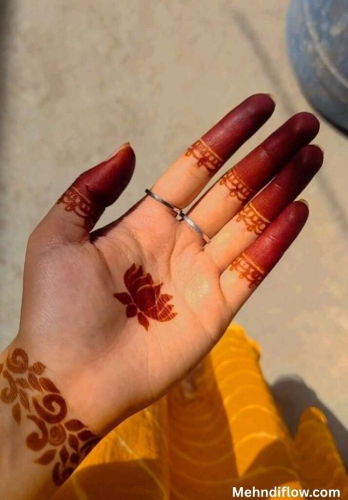 Simple single lotus henna design on the palm paired with solid stained fingertips and a patterned wrist cuff.